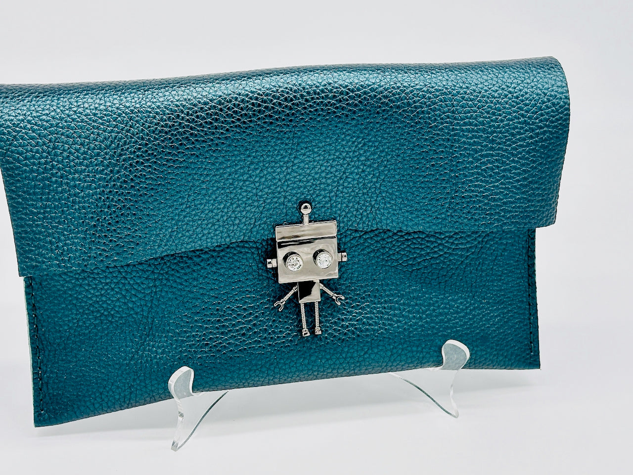Metallic green leather clutch bag with a robot clasp on a white stand