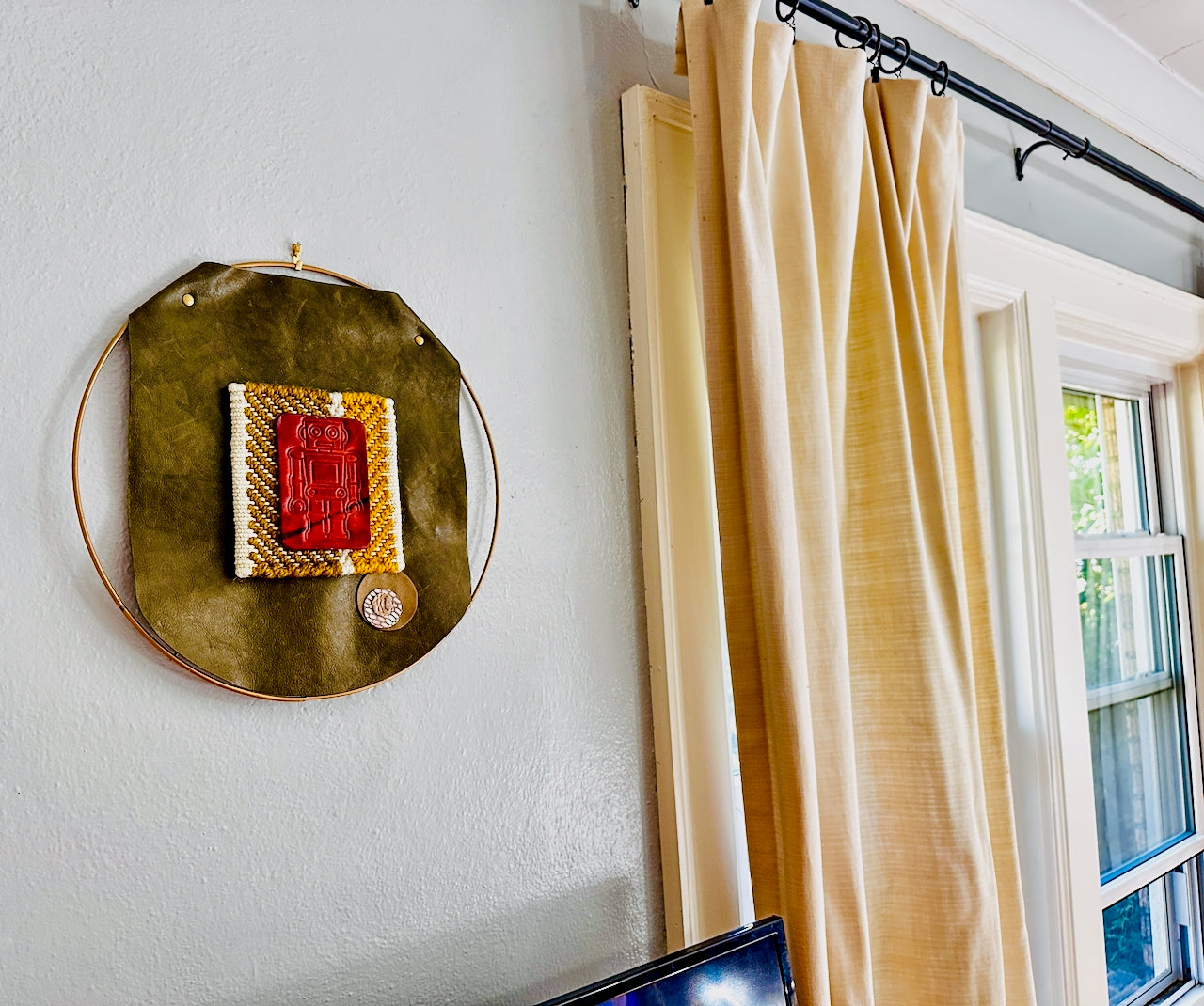 Decorative wall piece on a white wall next to a window with beige curtains.