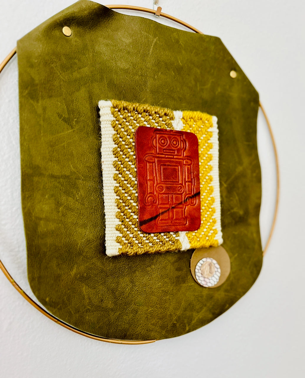 Textile art piece with a brown rectangular robot on a green leather background
