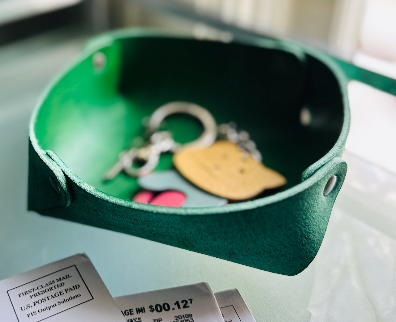 Green leather trinket dish with keys and a keychain on a glass surface.
