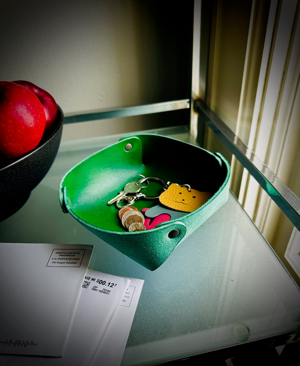 Green rounded squared dish with keys and cat keychain on a glass surface.