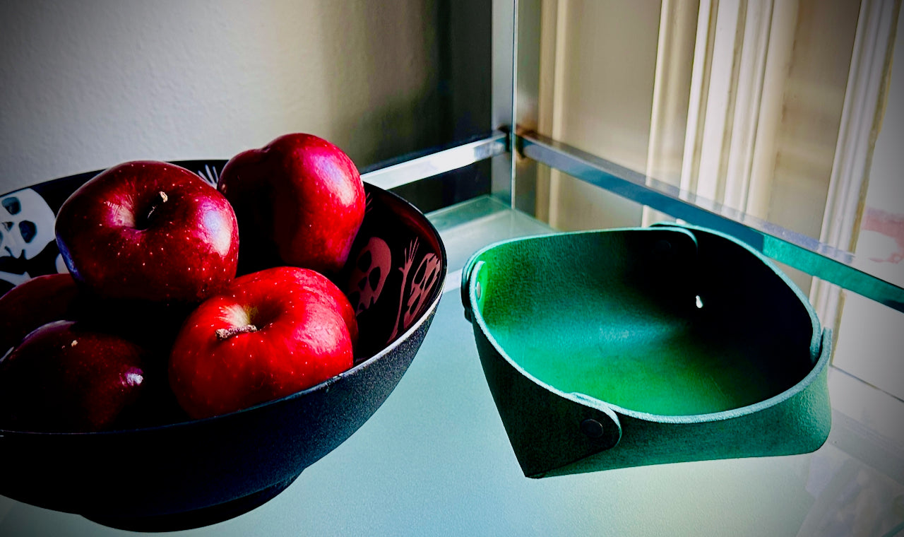 Bowl of red apples on a reflective surface with a green leather valet tray next to it.