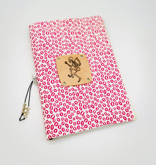Front cover of leather journal featuring a dancing skeleton on a background of pink lipstick kisses