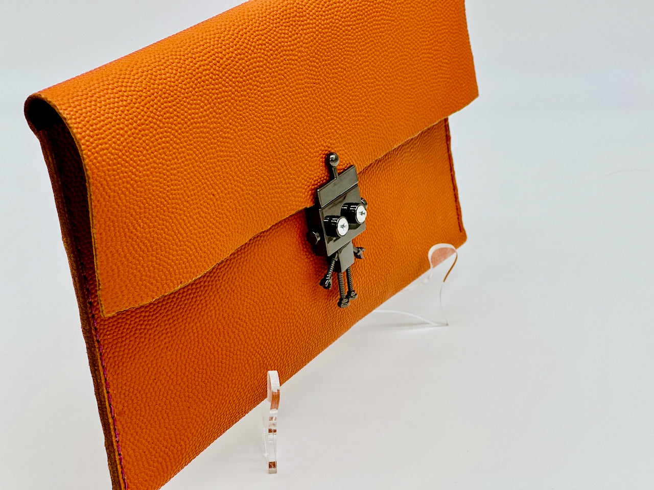 Orange clutch bag with a gun metal black silver robot clasp on a white background