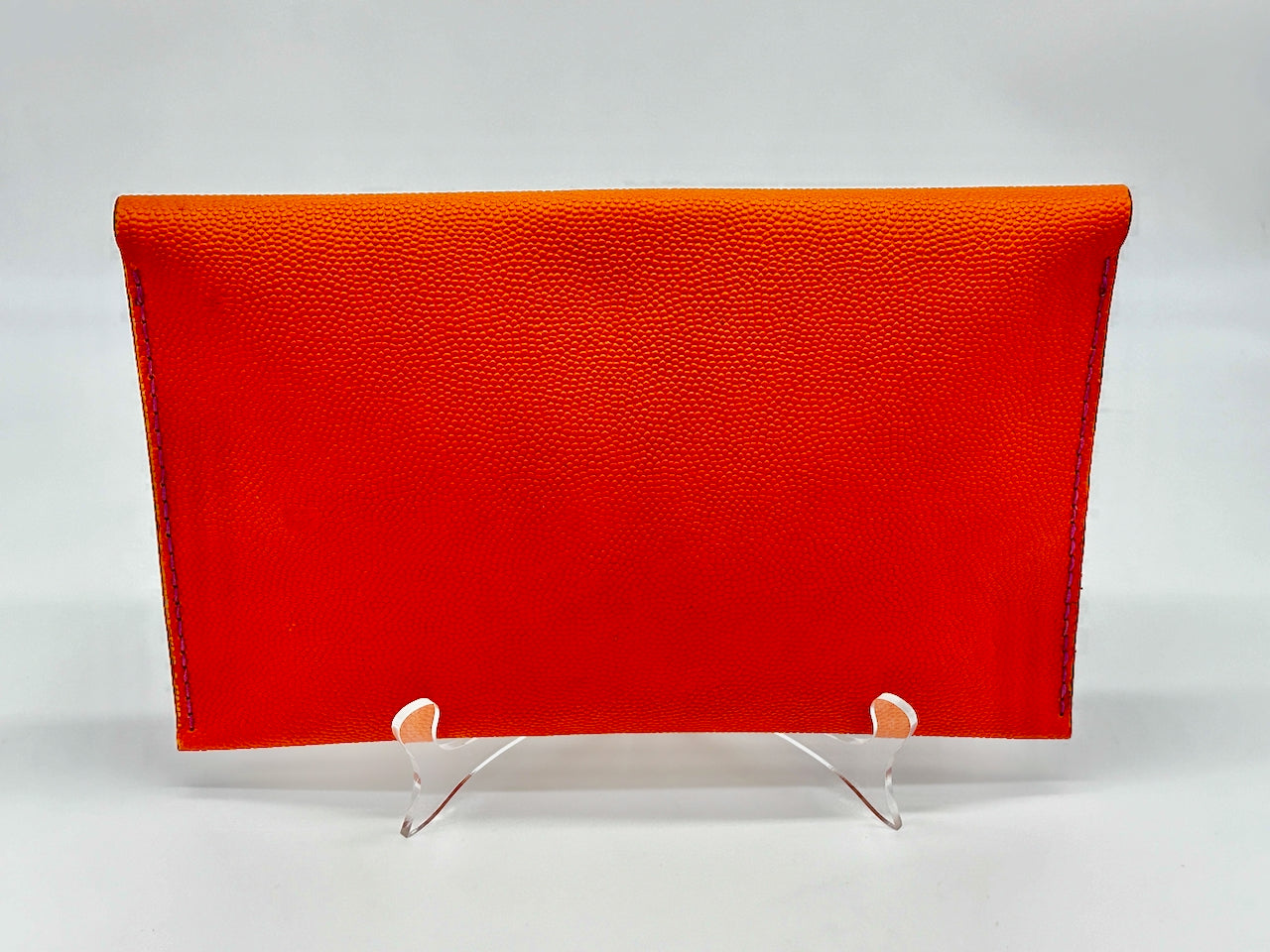 Orange clutch bag on a white stand against a white background
