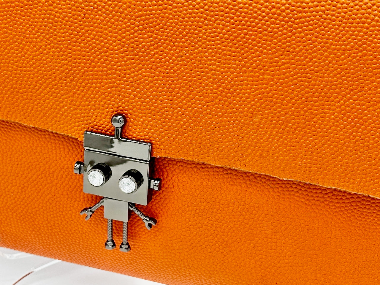 Metallic robot lock clasp on an orange textured leather clutch purse