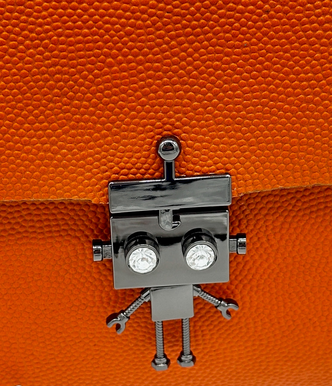 Metallic robot lock clasp on an orange textured leather clutch purse