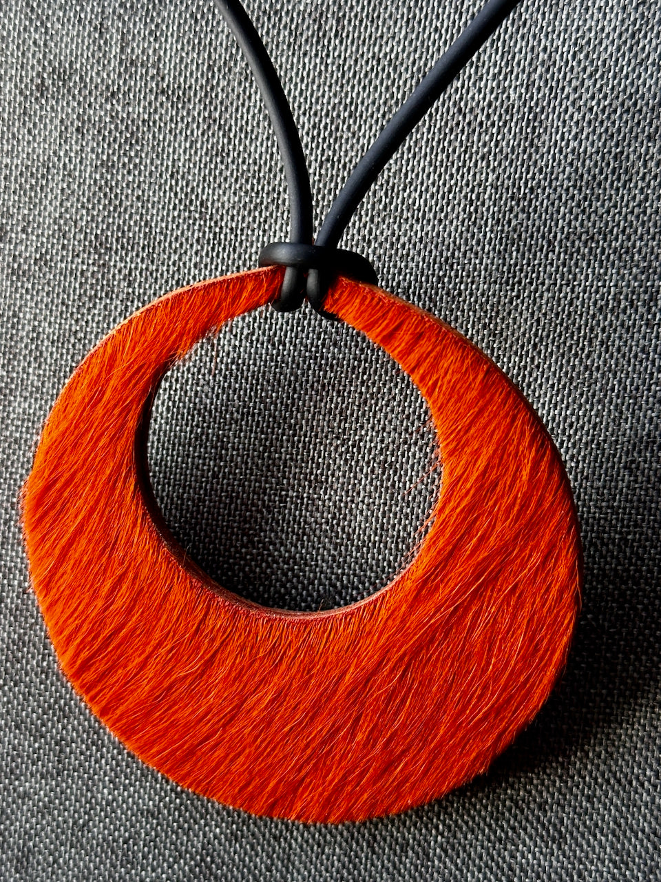 Orange circular hair on hide leather pendant necklace on a gray fabric background