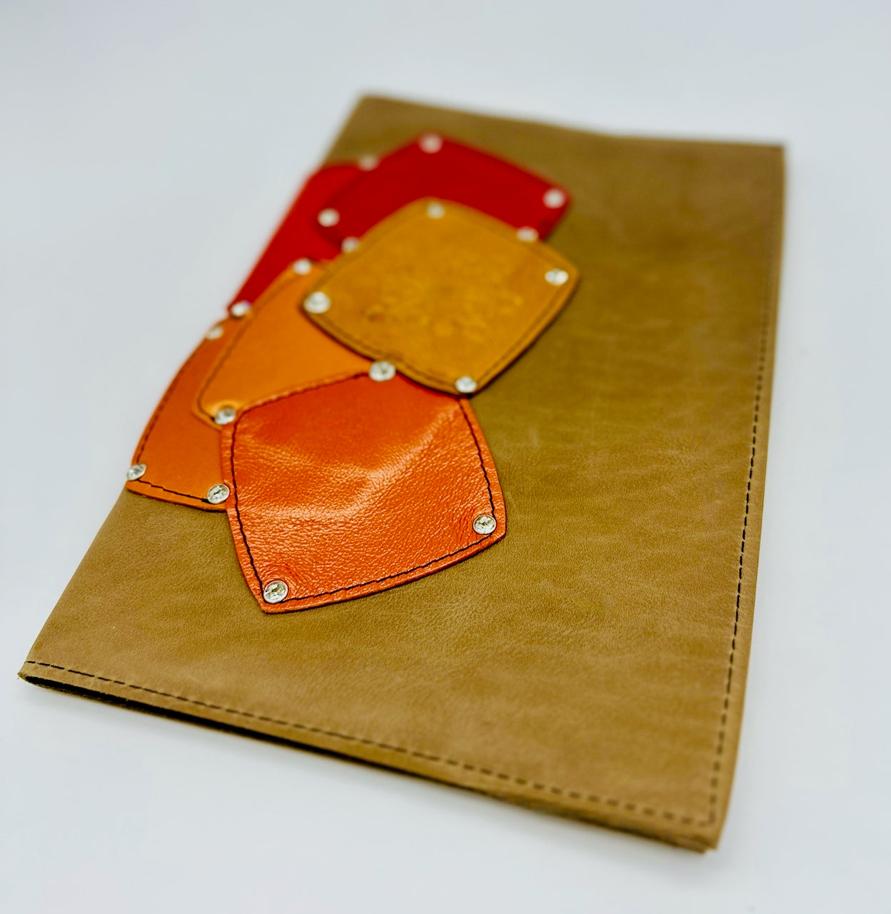 Tan brown leather notebook with orange, yellow and red patches on a white background