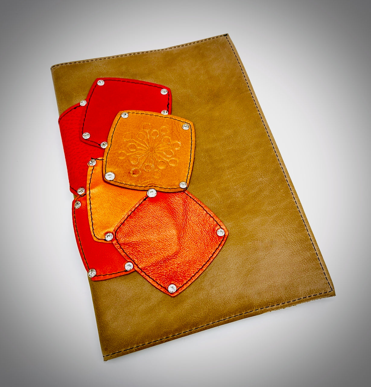 Tan leather notebook with red and orange patches on a gray background