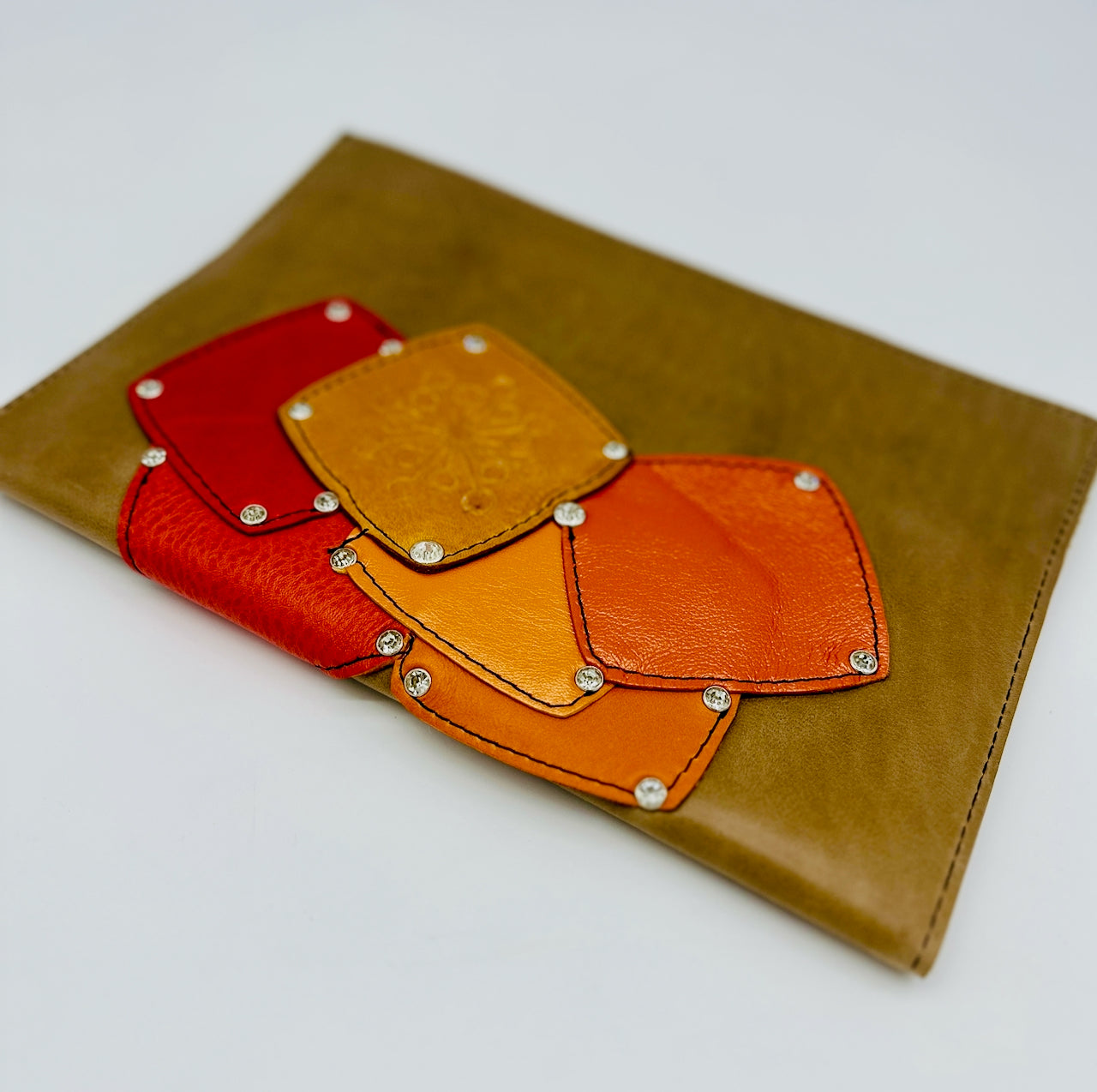 Tan leather pouch with red, orange, and yellow patch collage on a white background