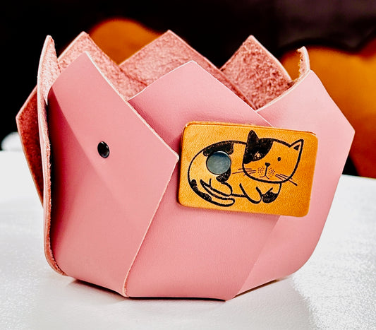 Pink riveted leather origami-style plant container with a cat illustration on tan leather.