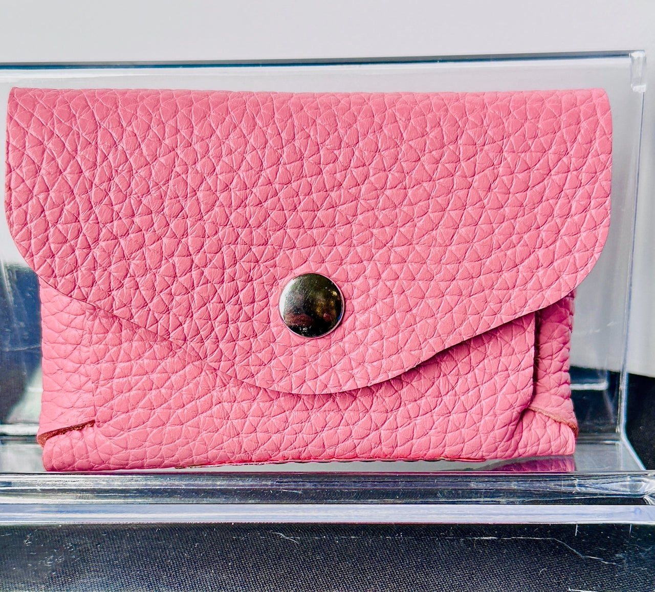 Pink textured wallet with a snap closure on a clear stand