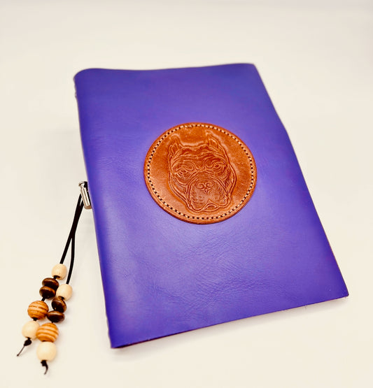 Purple leather refillable notebook with a brown leather patch featuring a dog's face, with a beige and brown wood toggle.