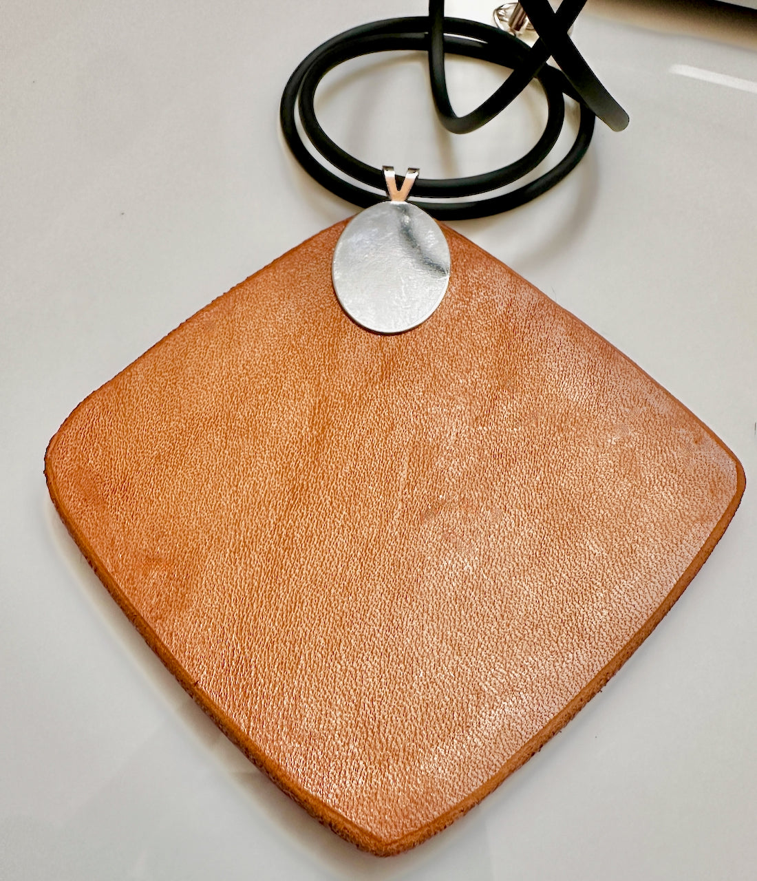 Natural veg tan leather backing on necklace with a silver bail on a white surface