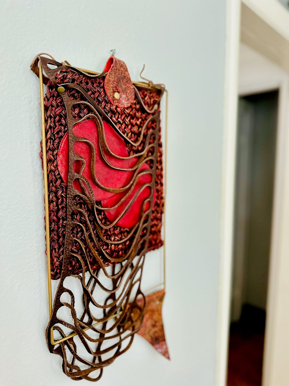 Decorative wall piece with red and brown leather and textiles on a white wall