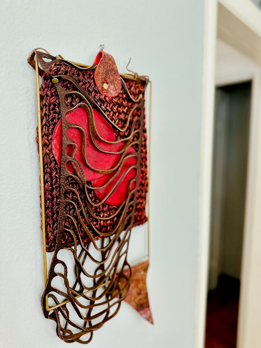 Decorative wall piece with red and brown leather and textiles on a white wall