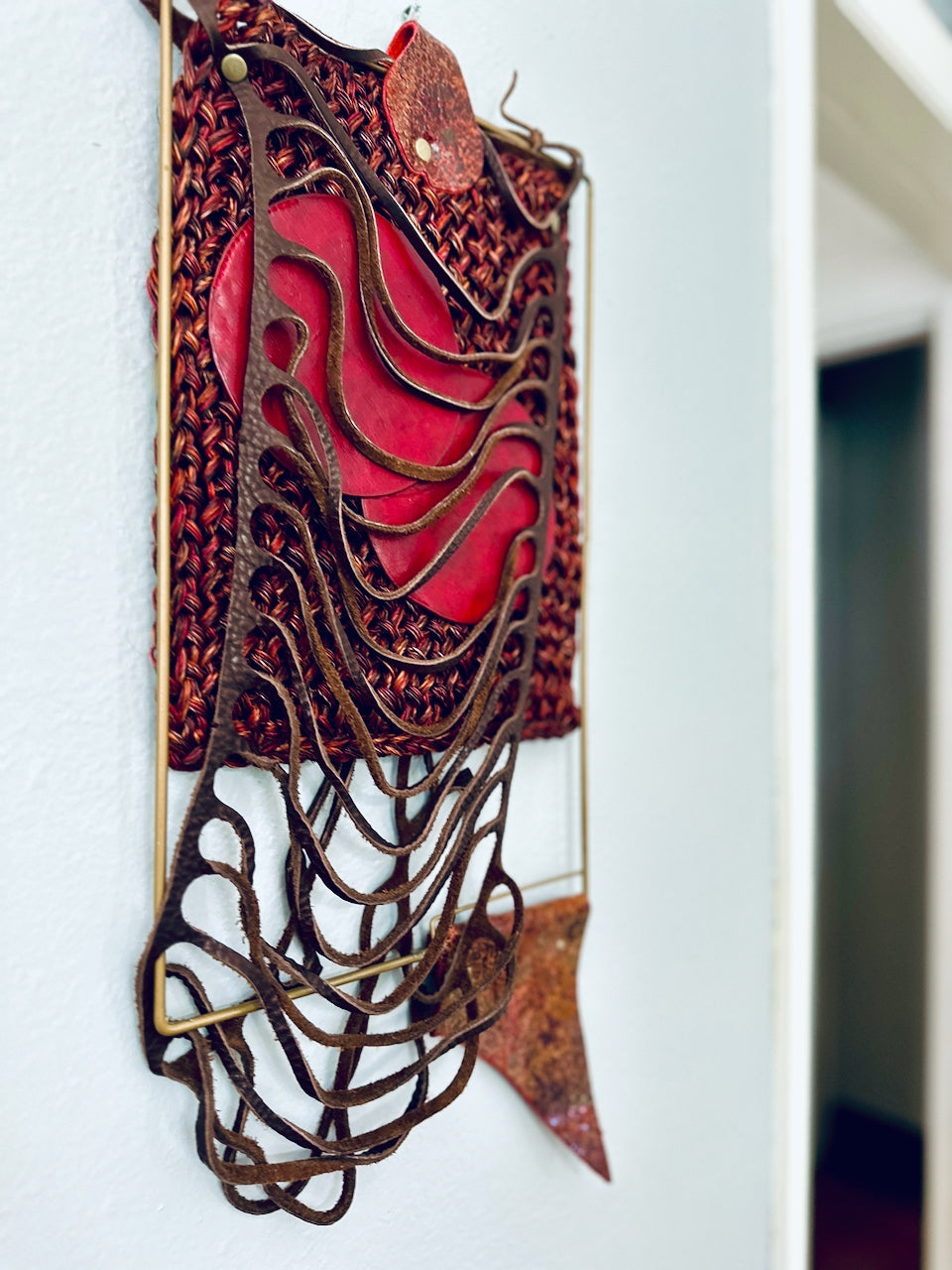 Decorative wall art with red central piece and brown leather on a white background