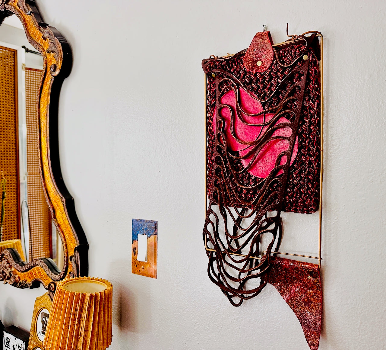 Decorative wall art with red and brown leather and textiles on a white wall.