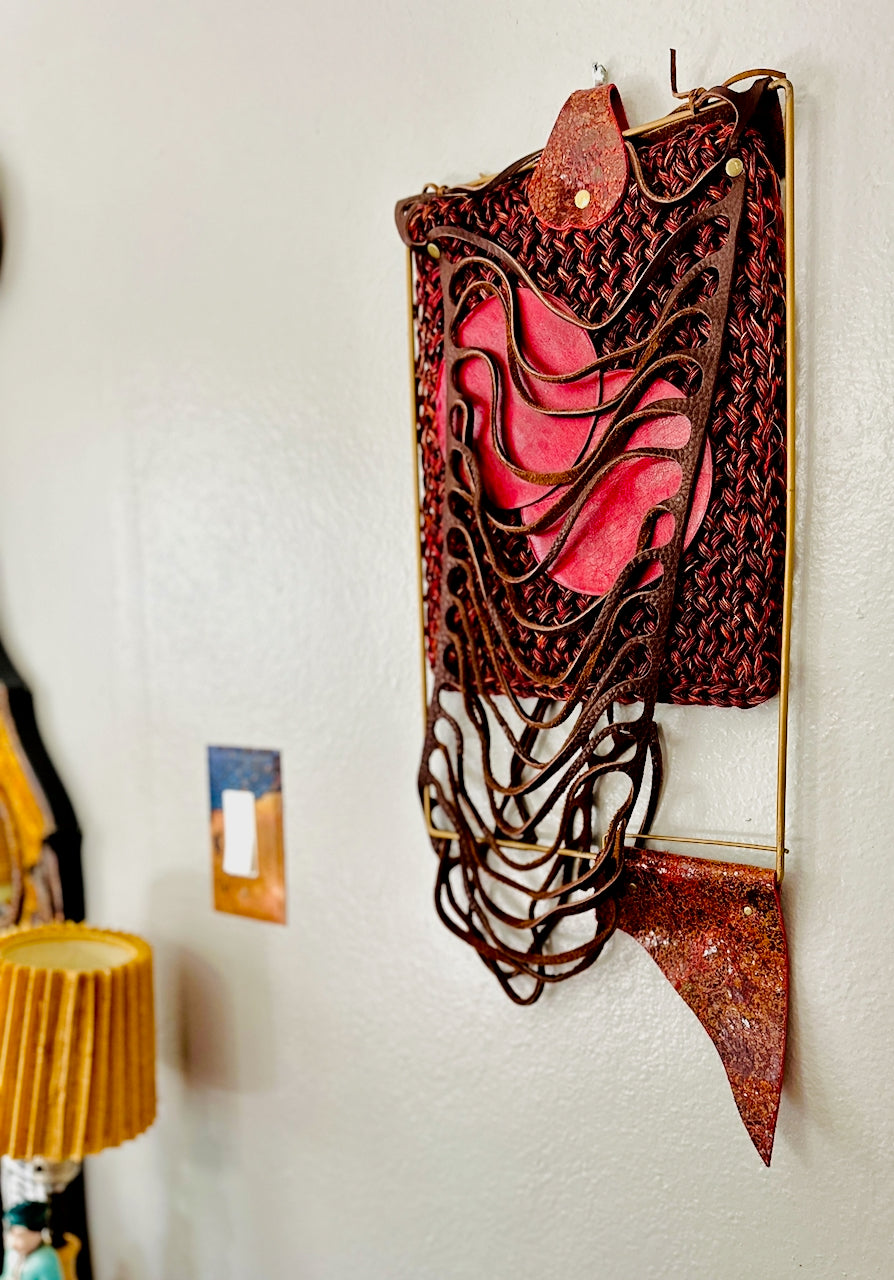 Decorative wall art piece with red and brown colors on a white wall.