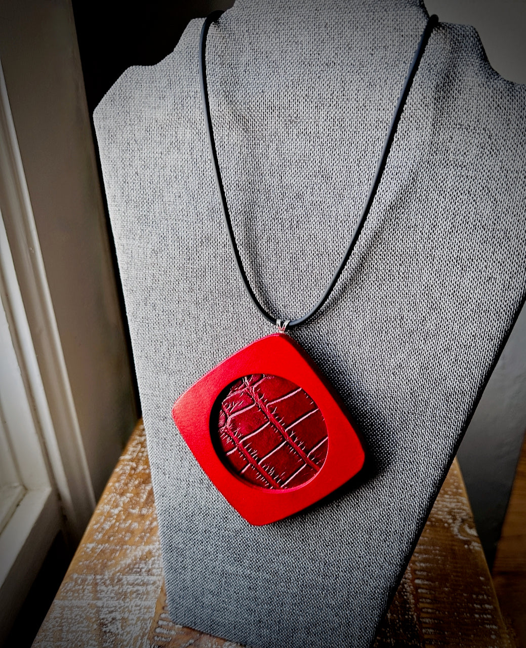 Red leather three layered pendant necklace on a gray mannequin bust