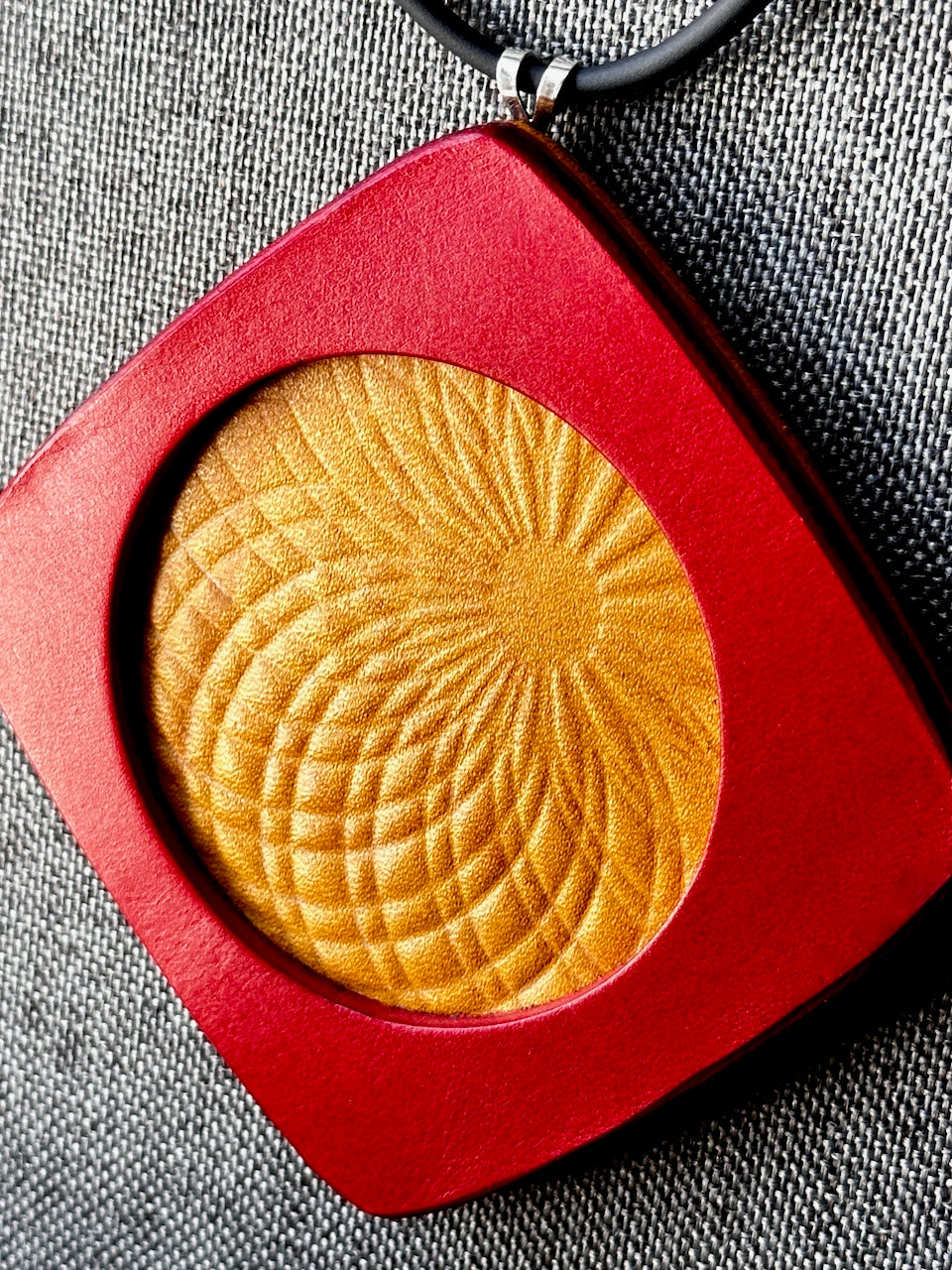 yellow and red circular pendant necklace in a red leather square frame on a gray background