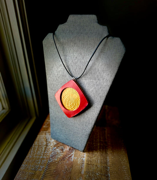 Necklace with a red and yellow embossed leather square pendant necklace on a gray bust against a dark background