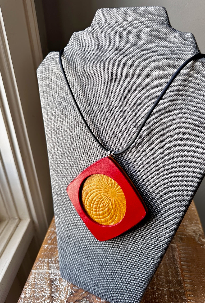 Necklace with a red and yellow embossed leather pendant necklace with rubber cording on a gray stand.