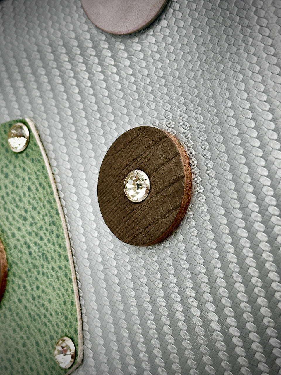 Close-up of a leather circle with a crystal rivet on a textured silver leather background