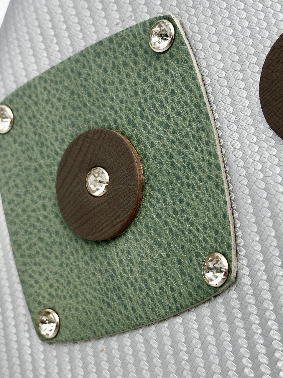Green leather rounded square patch with grey leather center and rhinestone rivets on a textured surface