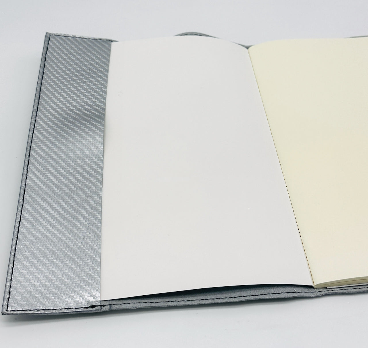 Open journal inside flap with carbon fiber leather pattern on one page and plain white on the other, on a light gray background.