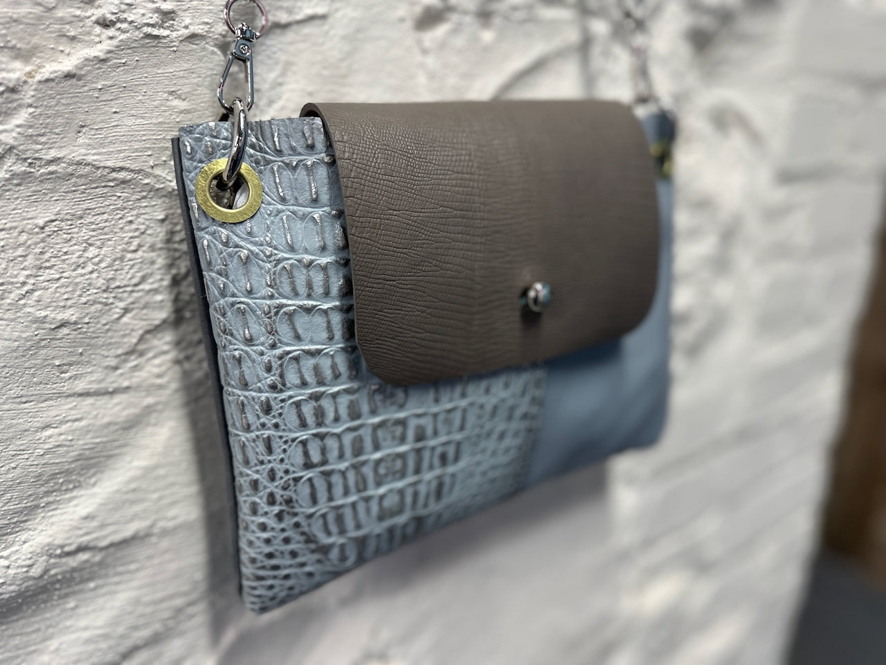 soft focus of blue crocodile embossed print leather purse with gray leather flap and silver closure hardware.
