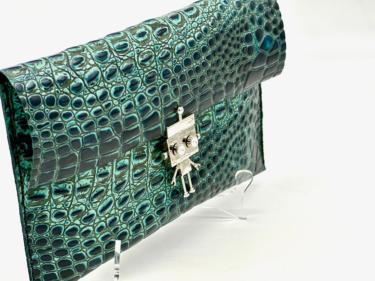 Green crocodile-patterned clutch bag with a silver robot clasp on a white background