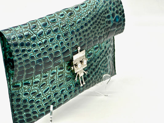 Green crocodile-patterned clutch bag with a silver robot clasp on a white background