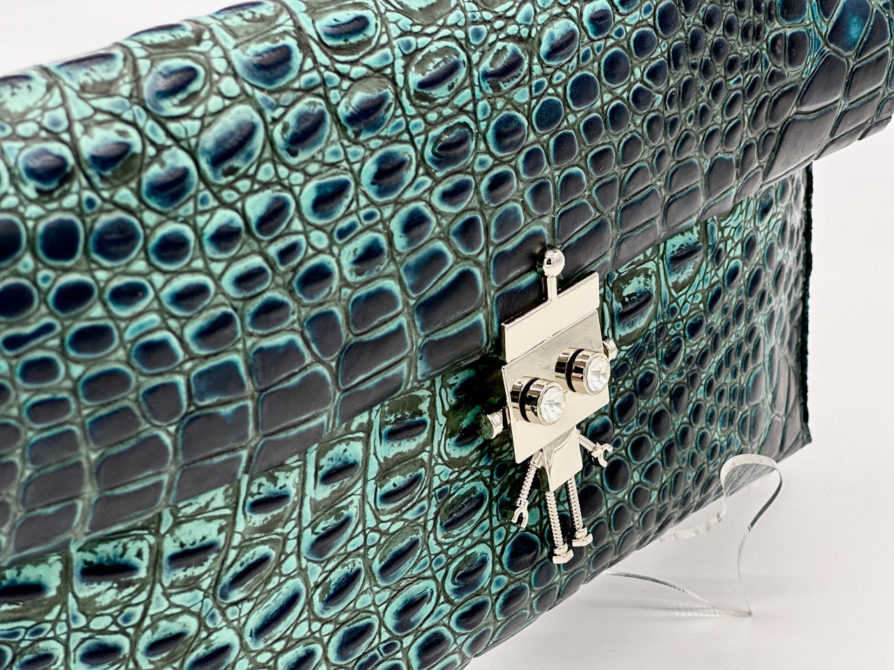 Green crocodile print leather handbag with a silver robot clasp on a white background