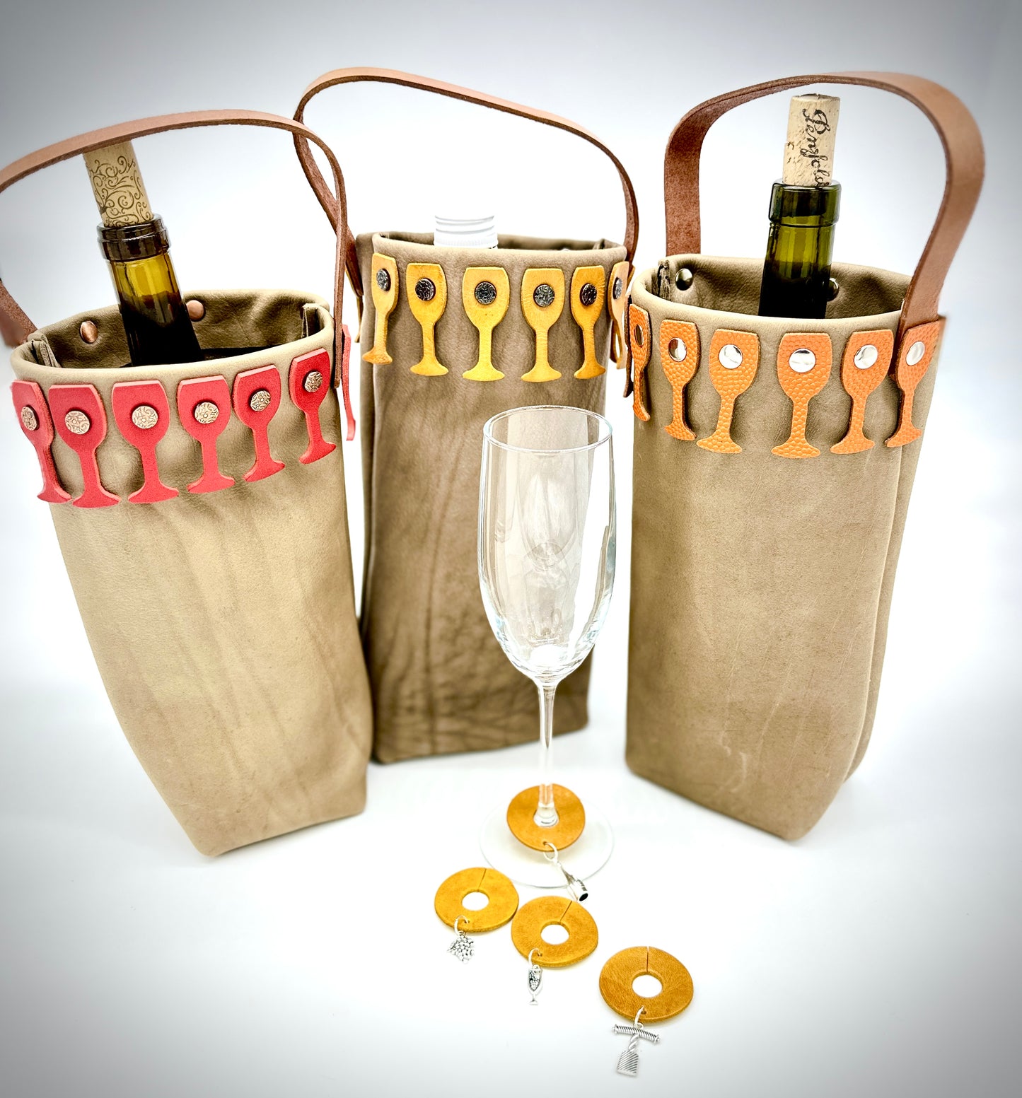 Three beige leather wine bags with decorative wine glass cutouts  and matching glass charms, on a white background