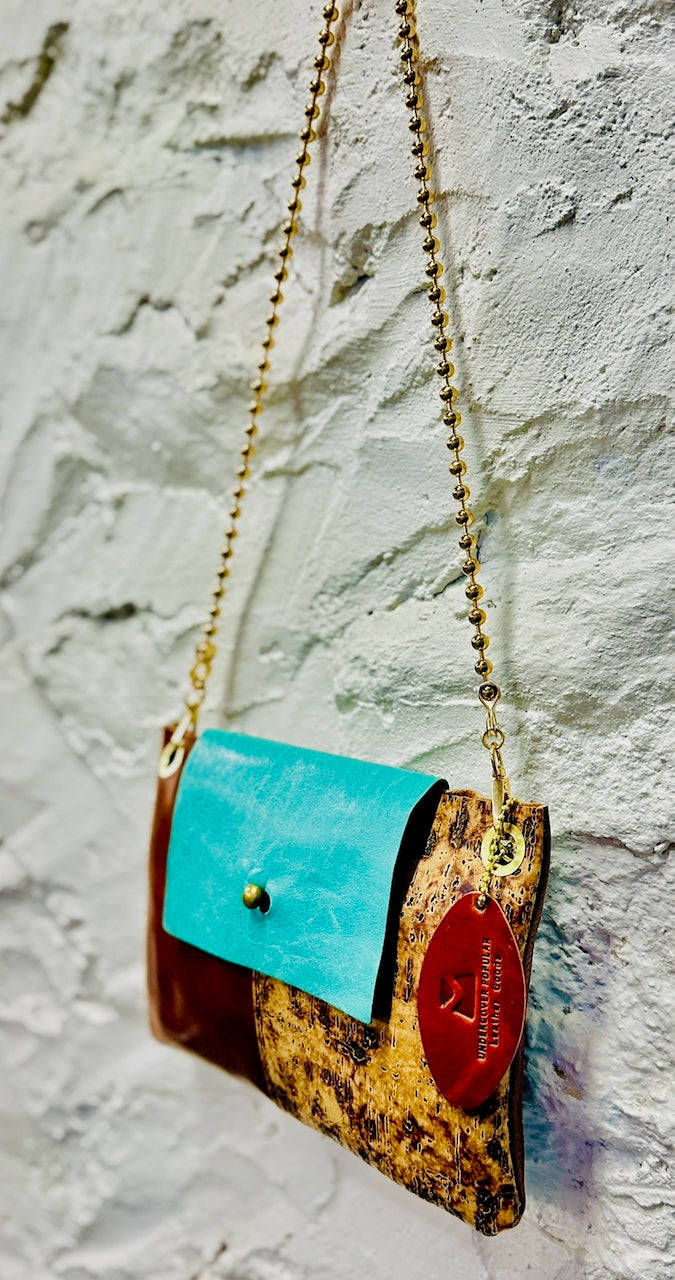 Turquoise blue, brown and cork leather purse hangs on white stucco wall
