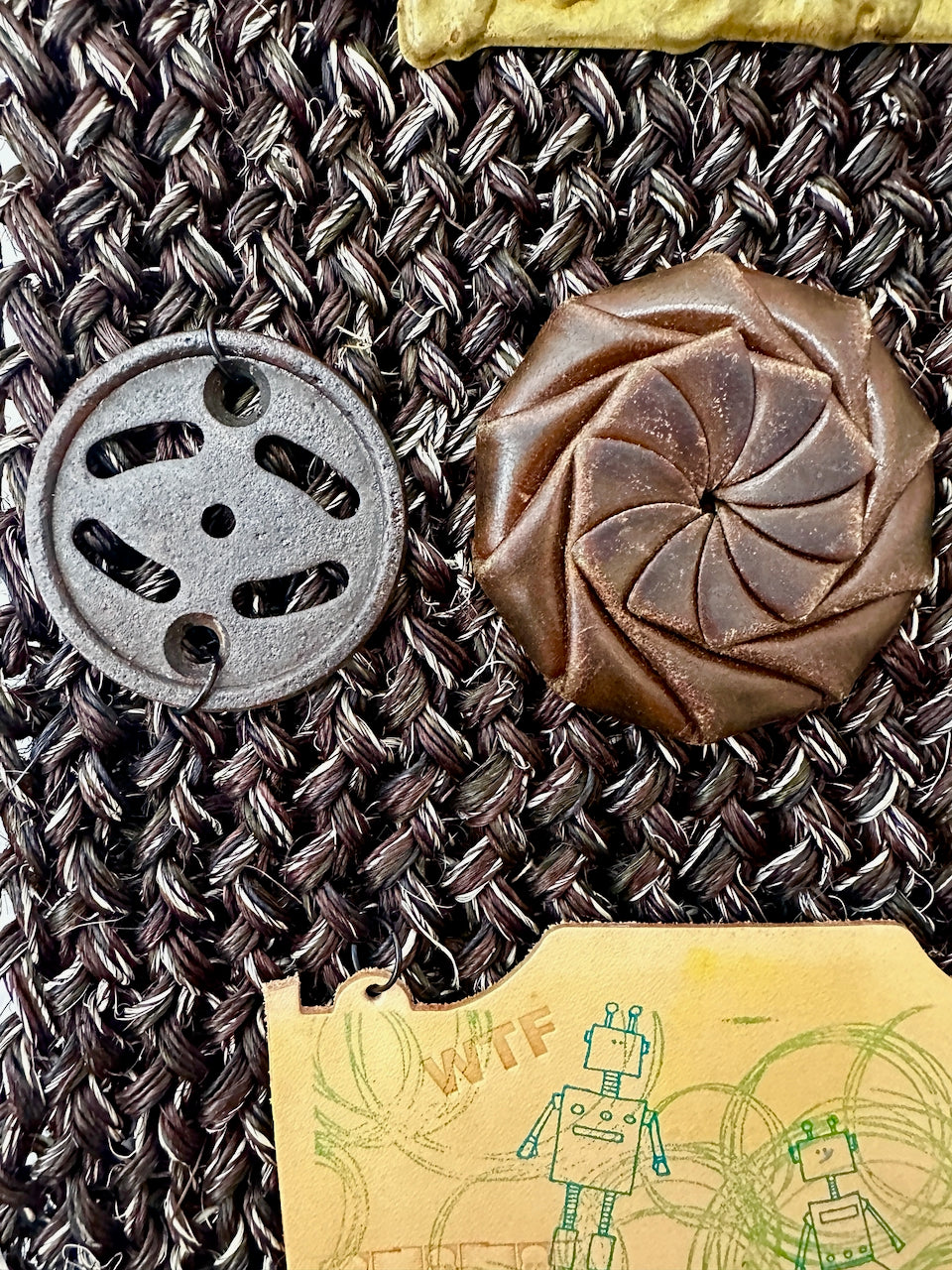 Decorative buttons and a small stamped leather patch with robot illustration on a textured fabric background