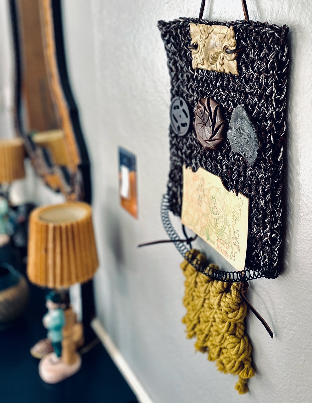 Decorative wall hanging with textured fabric and tassels on a white wall.