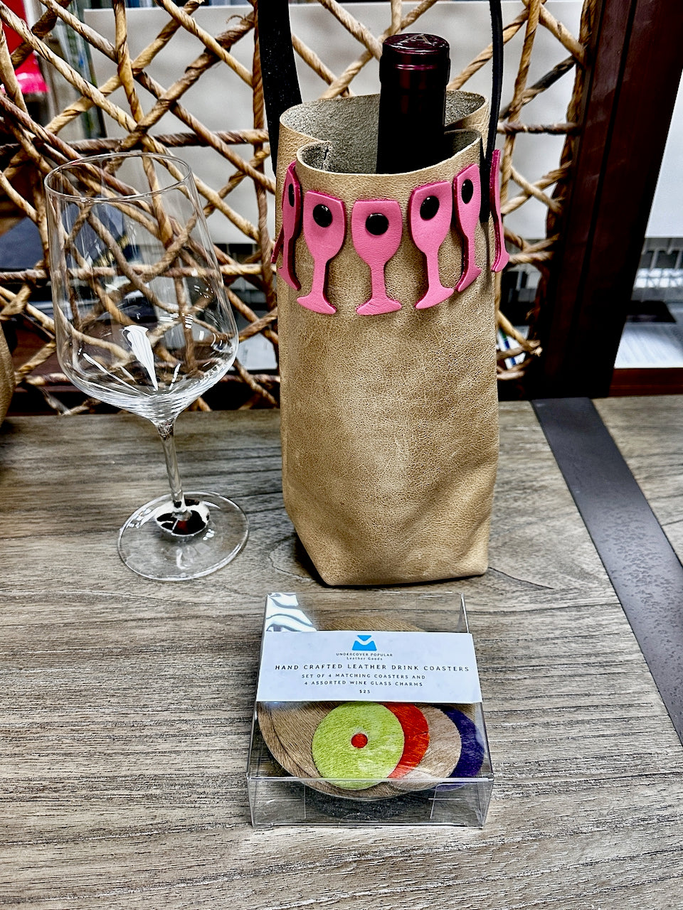 leather wine bottle carrier sits on table next to wine glass and box of wine charms