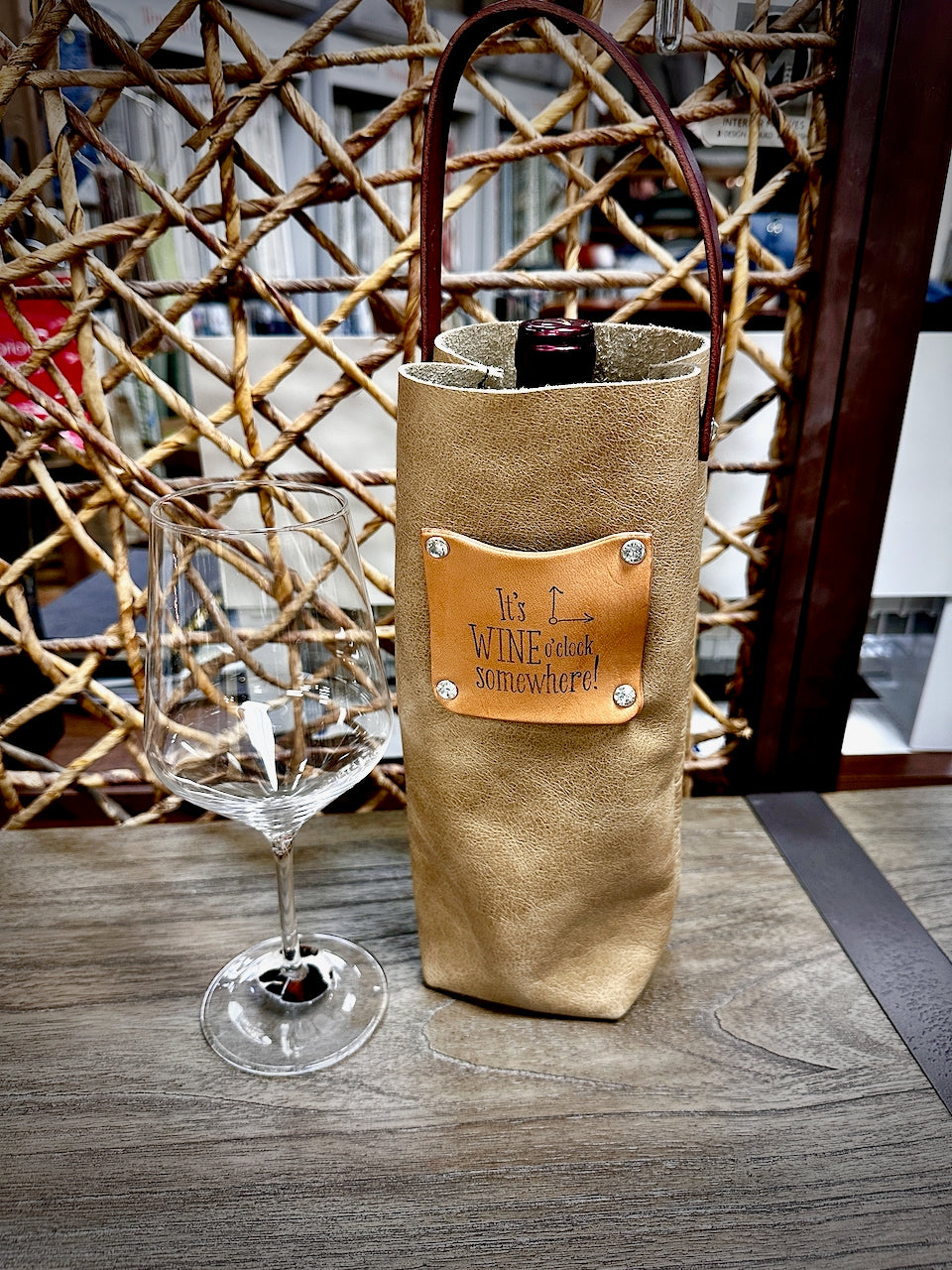 beige leather wine bottle carrier and wine glass on wood table