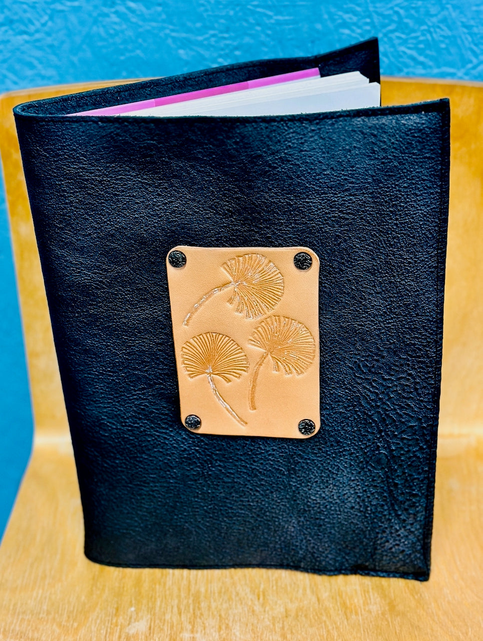 Black leather notebook with a embossed gingko leaves design on a wooden surface