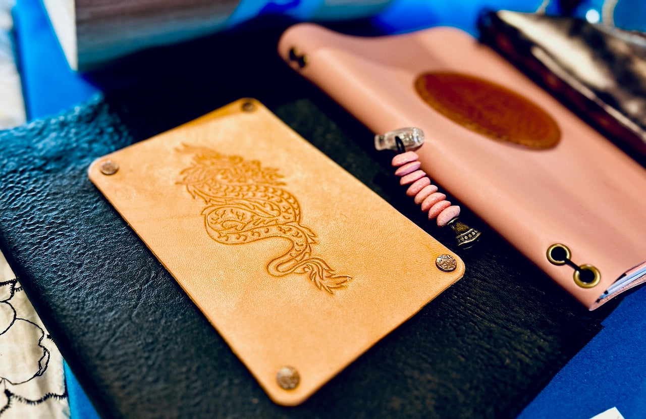 Close-up of a black leather journal with a dragon design on a blue surface.