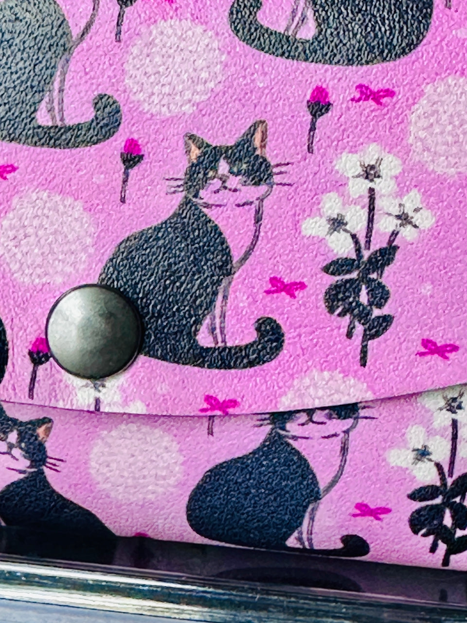 Closeup of pink wallet with black and white cats on it.