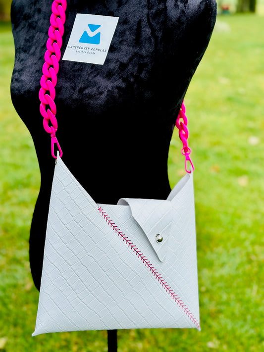 White leather crocodile embossed handbag with pink chain strap on a black mannequin against a grassy background