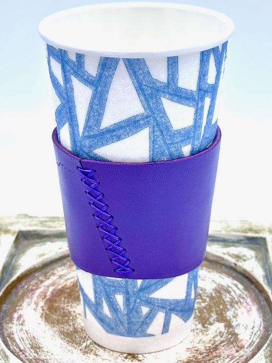 White paper cup with blue pattern and purple leather coffee sleeve.