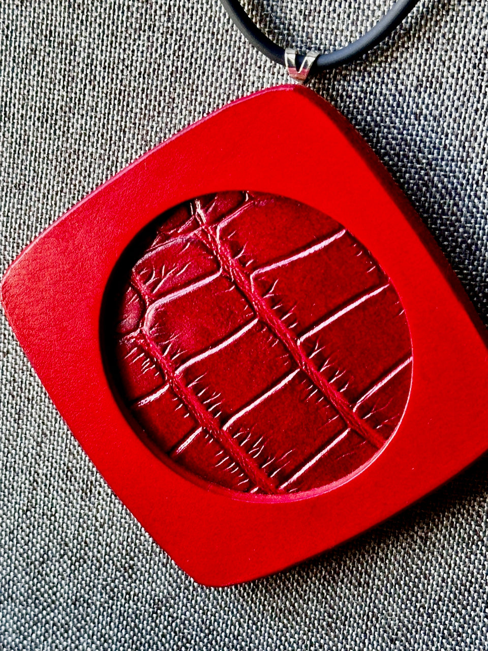 Red square leather pendant with embossed crocodile pattern on a gray fabric background