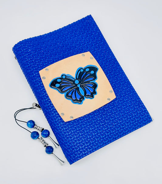 a bird's eye view of a handmade, leather bound journal with a refillable, lined paper insert featuring a butterfly.